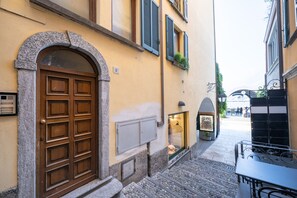 A narrow street with a stone archway leading to a building with a wooden door and shutters. - Charming Mella Apartment (Bellagio)