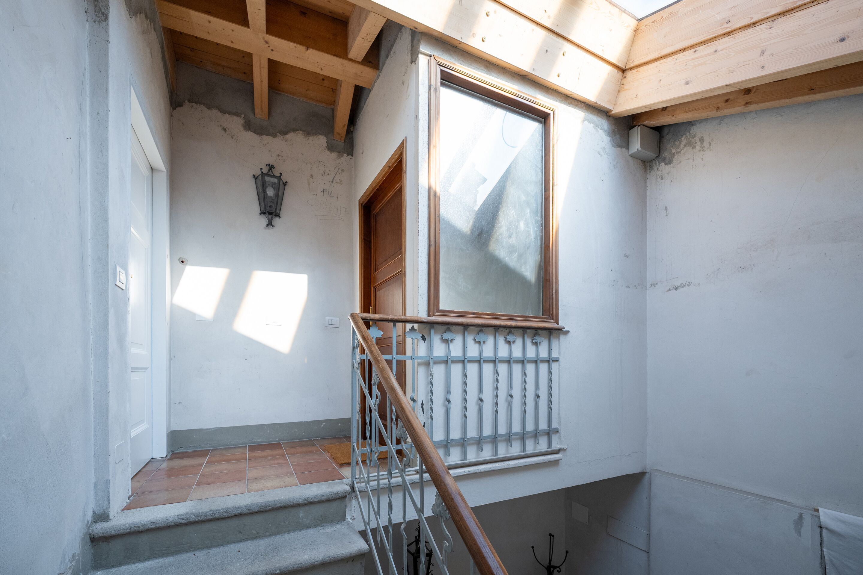 Una escalera con barandilla de madera, un ventanal con marco de madera y un aplique de pared.