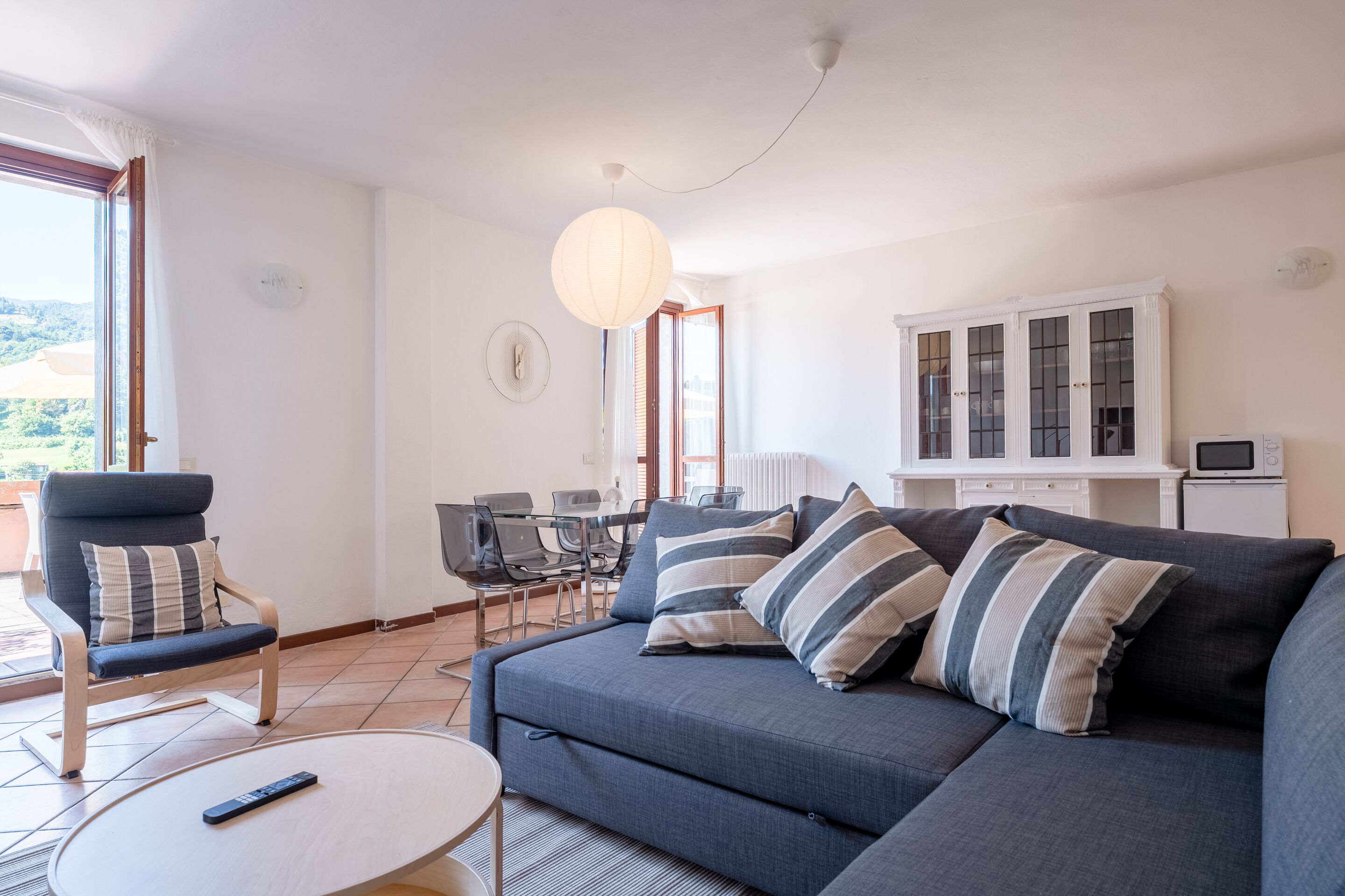 Ein modernes Wohnzimmer mit einer Eckcouch, einem Esstisch und Stühlen. Ein Fernseher steht auf einem Schrank und eine Fernbedienung liegt auf einem Couchtisch.