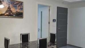 A dining area with a glass-top table and black chairs, a ceiling fan, a door with a lock, and a painting of the Eiffel Tower. - Escape to Eden heights,a 2 bedroom Apt with Gym access near the West Hills Mall. (Weija, Accra)