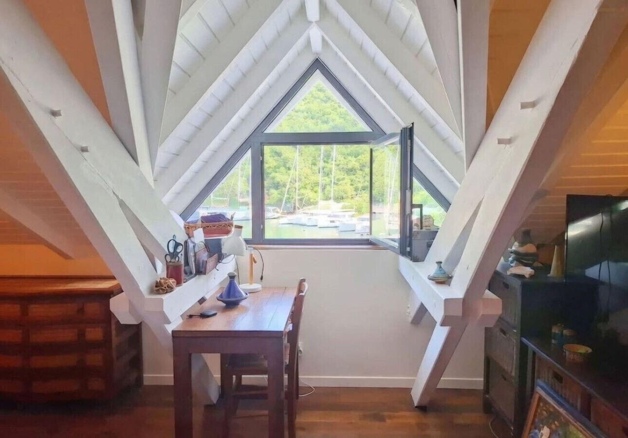 Ein Zimmer mit schragem Dach, einem Esstisch, Stühlen, einem Fernseher und einem Fenster mit Blick auf Boote.