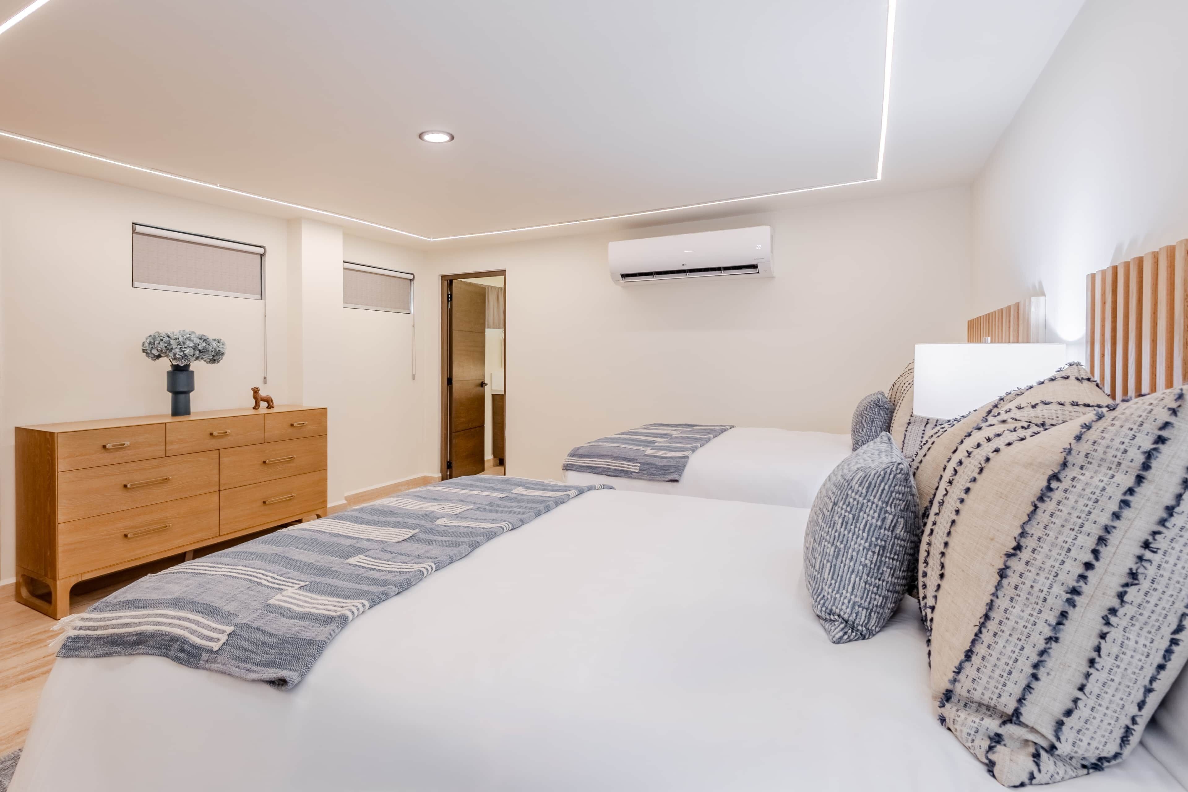 A modern bedroom with a large bed, a wooden dresser, and an air conditioning unit.