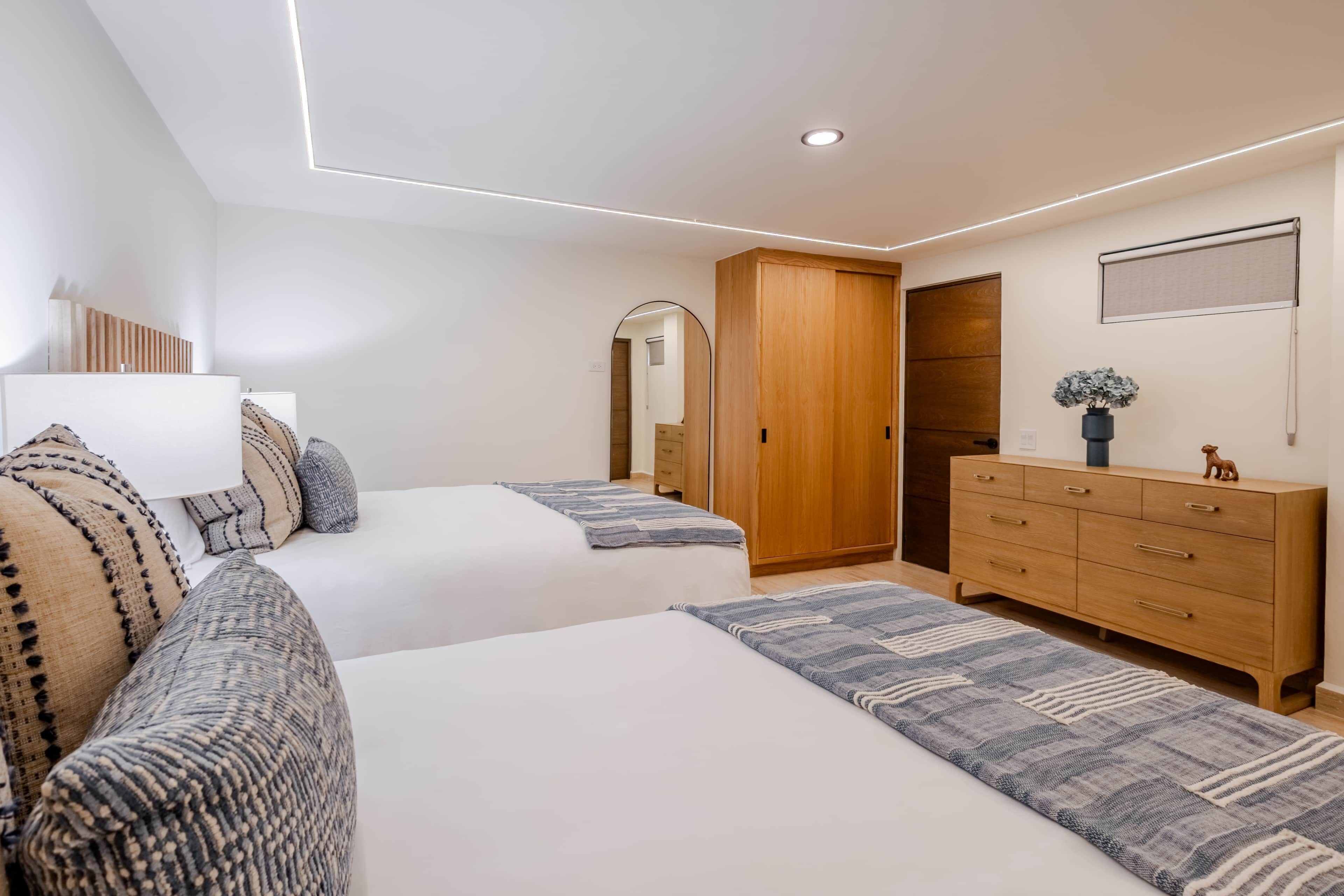 A bedroom with two beds, a dresser, a mirror, and a ceiling light fixture.