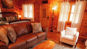 A cozy cabin interior with a brown leather sofa, a white armchair, and a wooden coffee table. - Secluded Cozy Log Cabin Villa (Creola)