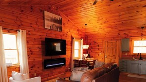 A log cabin interior with a living room, TV, sofa, and kitchen area. - Secluded Cozy Log Cabin Villa (Creola)