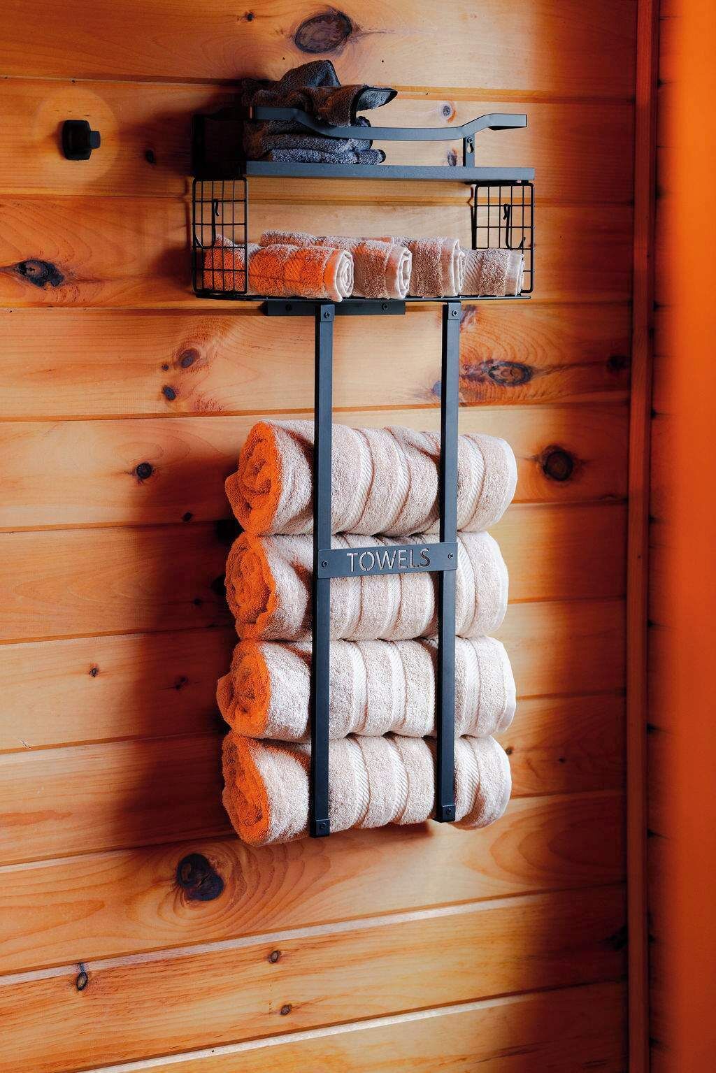 A wooden wall with a towel rack holding rolled towels and a small shelf with a towel and a cup.