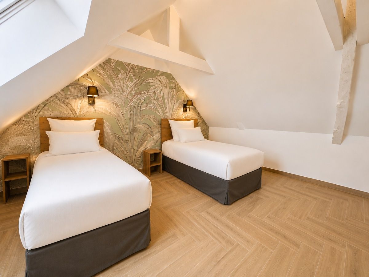 Quarto com duas camas, teto inclinado e parede com padrão de folha.