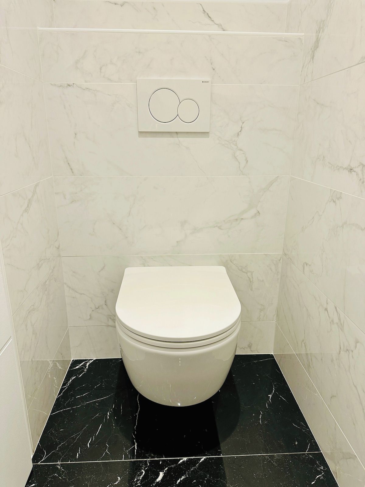 Eine Toilette in einem Badezimmer mit weißen Marmorfliesen und einem schwarzen Marmorboden.