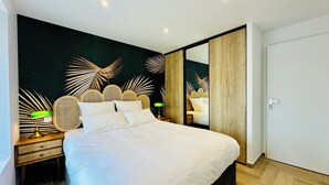 A modern bedroom with a large bed, a nightstand with a lamp, a mirror, and a dark wall with leaf patterns. - La Bastide du Causse - Domaine Gouloumès (Ginouillac)