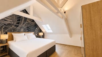 A bedroom with a bed, bedside tables, a nightstand, a wooden wardrobe, and a sloped ceiling with a skylight.