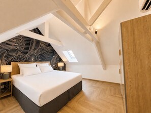 A bedroom with a bed, bedside tables, a nightstand, a wooden wardrobe, and a sloped ceiling with a skylight. - La Bastide du Causse - Domaine Gouloumès (Ginouillac)