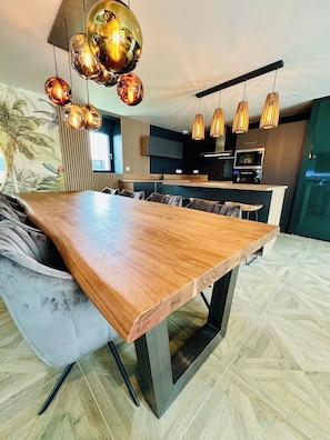 A modern kitchen with a central island, pendant lighting, and a dining area with a large wooden table. - La Bastide du Causse - Domaine Gouloumès (Ginouillac)