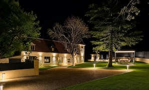 A stone house with a well-lit driveway, a covered outdoor dining area, and a lawn. - La Bastide du Causse - Domaine Gouloumès (Ginouillac)