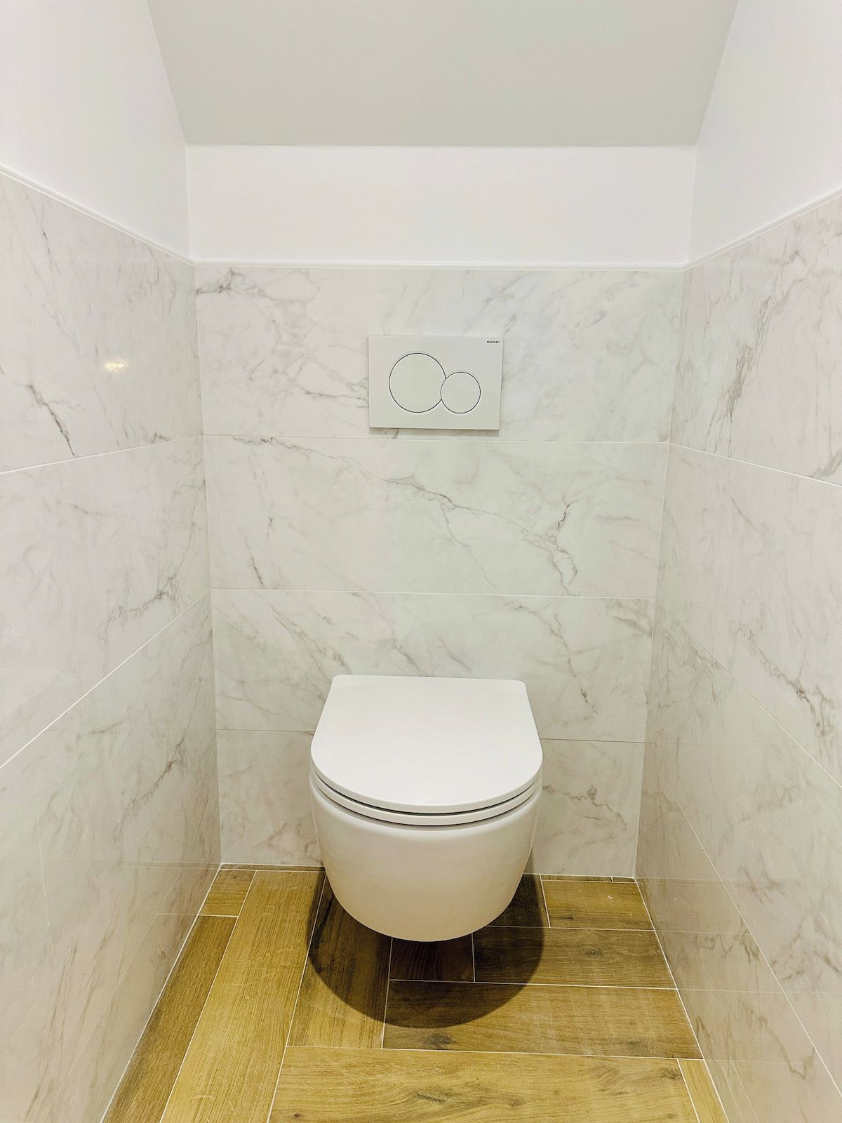A bathroom with a toilet, marble walls, and a wooden floor.