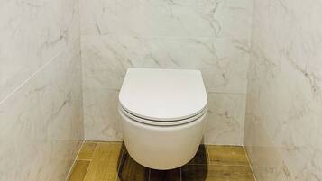 A bathroom with a toilet, marble walls, and a wooden floor.