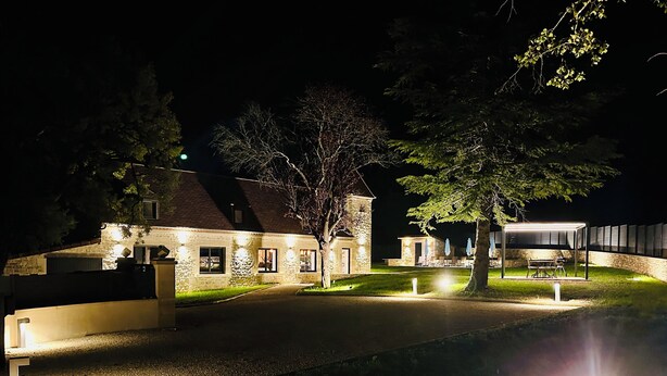 A stone building with a paved driveway, outdoor seating, and a covered area with a grill. - La Bastide du Causse - Domaine Gouloumès (Ginouillac)