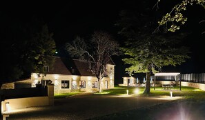 En bygning i sten med en belagt indkørsel, udendørs siddepladser og et overdækket område med grill.