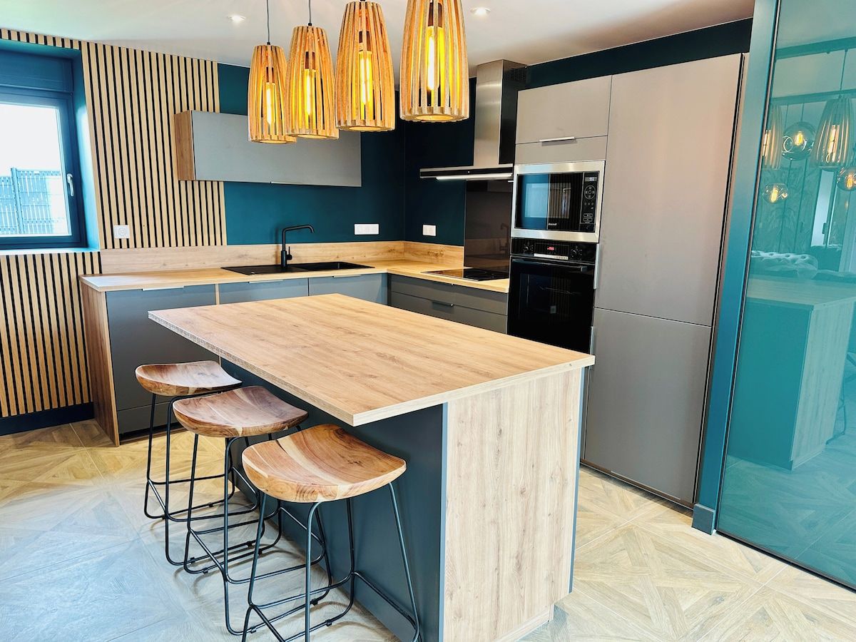 Une cuisine moderne dotée d’un îlot central, de tabourets de bar, de luminaires suspendus et d’appareils électroménagers intégrés.
