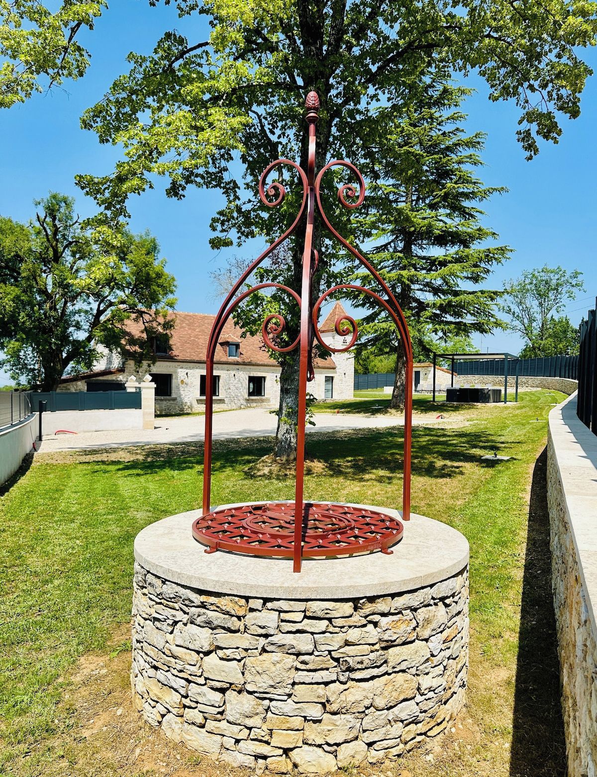 Une structure circulaire en pierre, dotée d’un escalier en colimaçon métallique, entourée d’herbe et d’arbres.