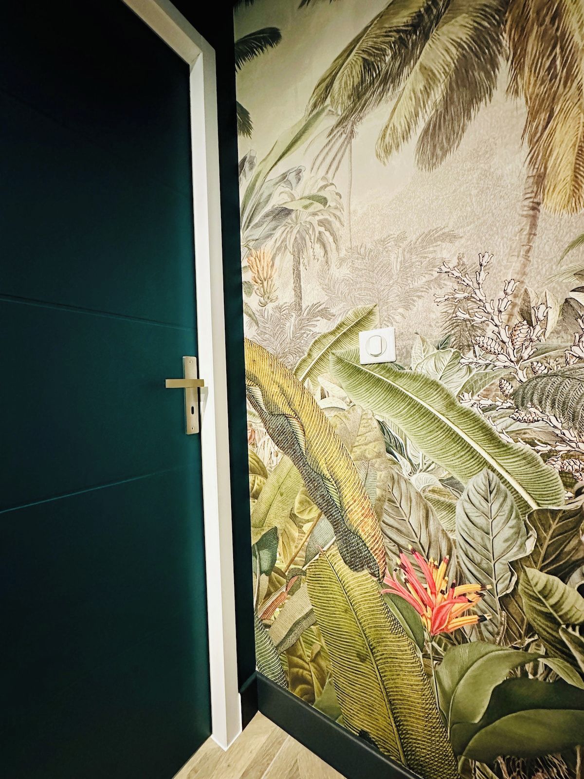 Habitación con puerta verde y un mural en la pared que muestra follaje tropical.
