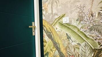 Habitación con puerta verde y un mural en la pared que muestra follaje tropical.