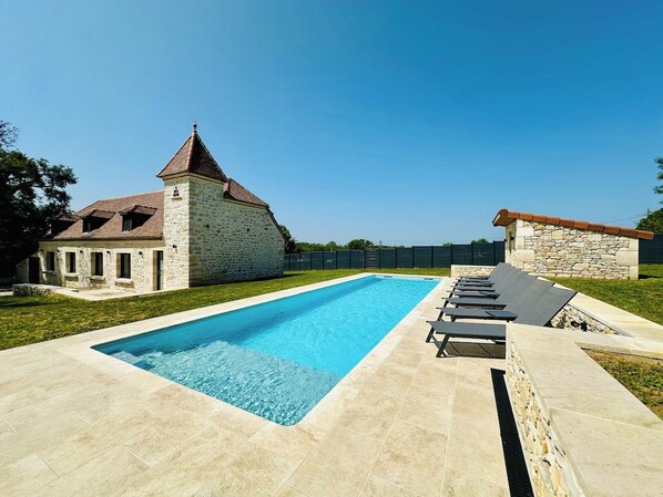 A swimming pool with lounge chairs, stone buildings, and a clear sky.