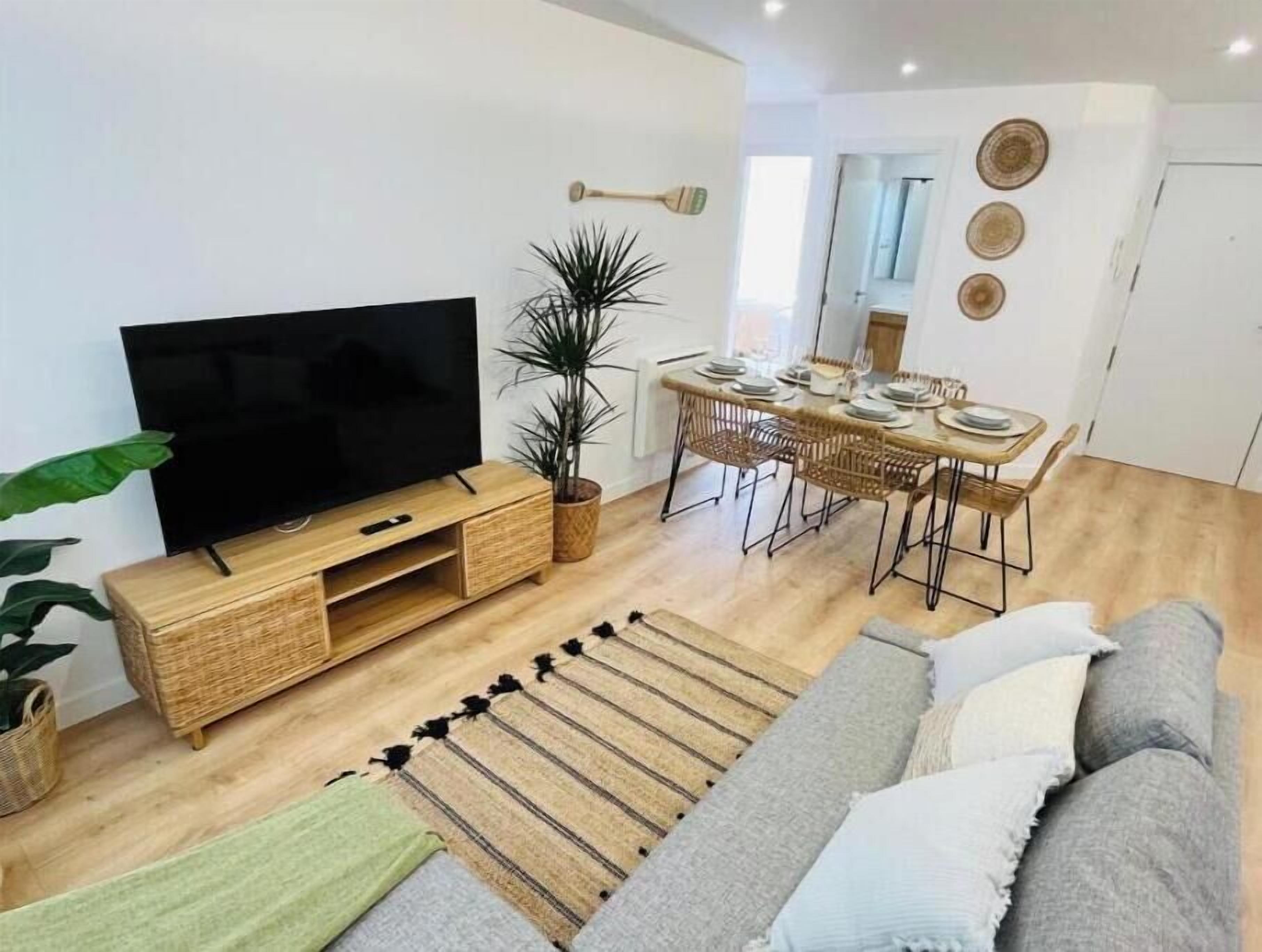 A modern living room with a flat-screen TV, a dining area with a table and chairs, a sofa, and a potted plant.