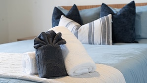 Ein ordentlich bezogenes Bett mit einer blauen Tagesdecke, einer weißen Decke und einem aufgerollten Handtuch.