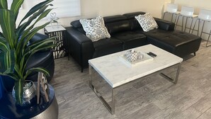 Ein modernes Wohnzimmer mit einem schwarzen Ledersofa, einem weißen Couchtisch und einer Topfpflanze.