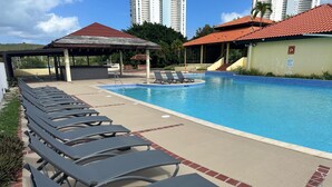 Ein Swimmingpool mit Liegestühlen, einer überdachten Pergola und einem Gebäude mit roten Ziegeln.