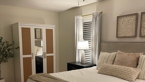 Un dormitorio con cama, mesita de noche, armario, ventilador de techo y ventana con cortinas.