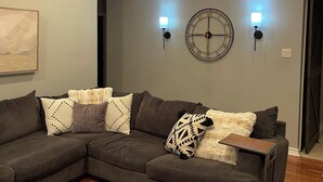 Una sala de estar moderna con un sofá seccional, una araña, luces empotradas en la pared y un reloj.