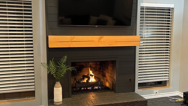 Una chimenea moderna con un televisor encima, flanqueada por dos ventanas con persianas.