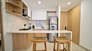 Een moderne keuken met een centraal eiland, houten krukken, een koelkast en witte kasten.