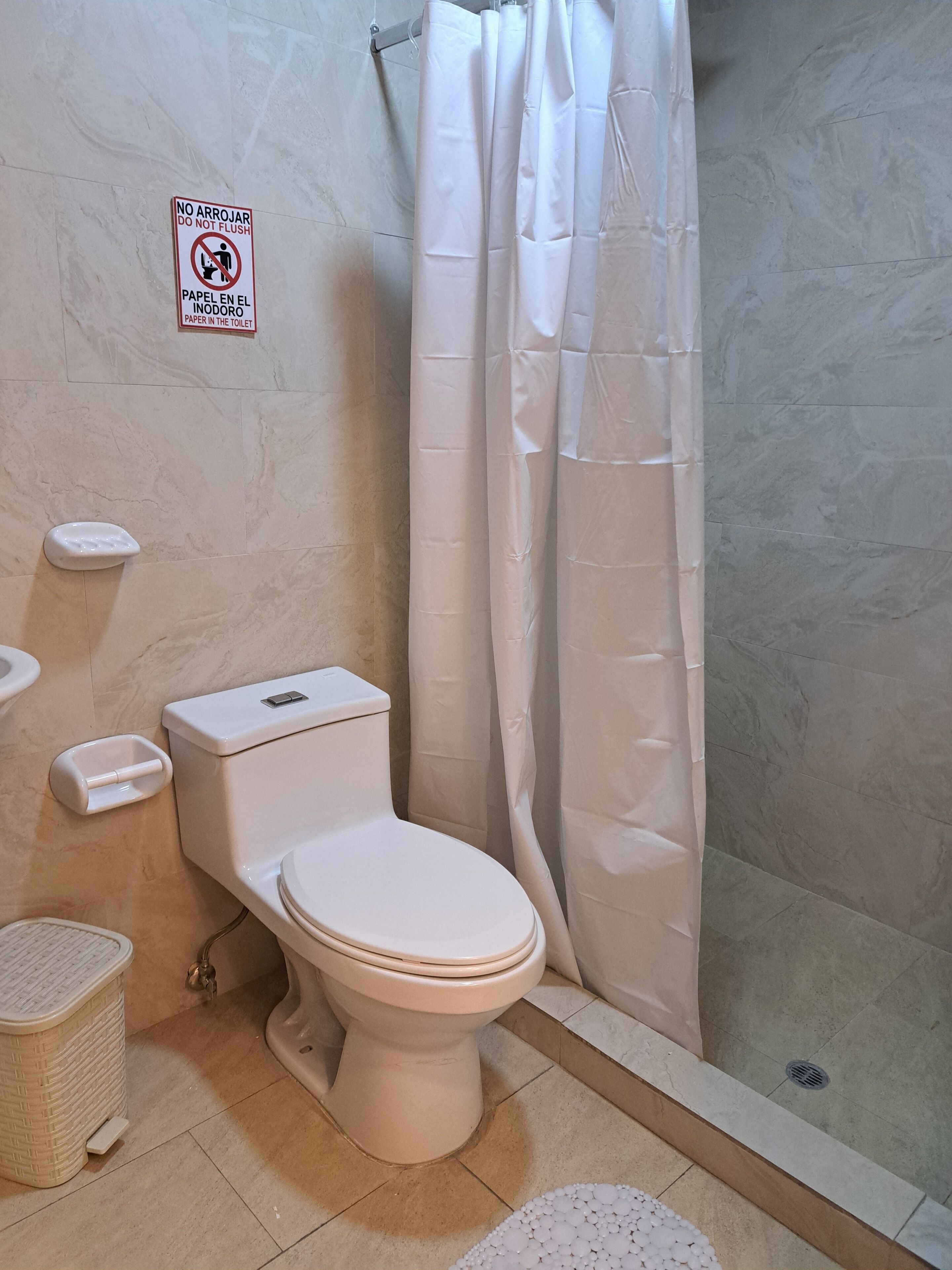 Une salle de bain équipée de toilettes, d’un rideau de douche et d’un panneau indiquant qu’il est interdit de jeter du papier dans les toilettes.