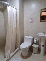 Un baño con inodoro, lavamanos, cubo de basura y cortina de ducha.