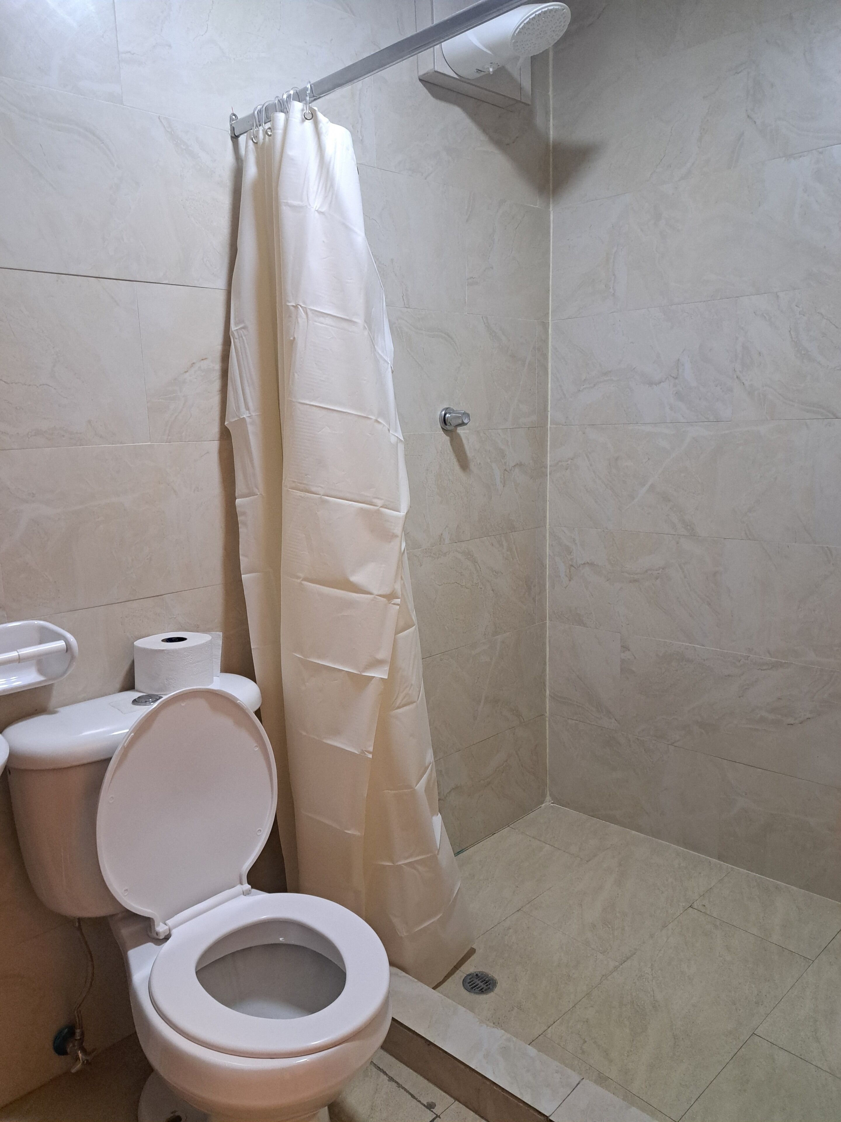 A bathroom with a shower, toilet, and a roll of toilet paper.