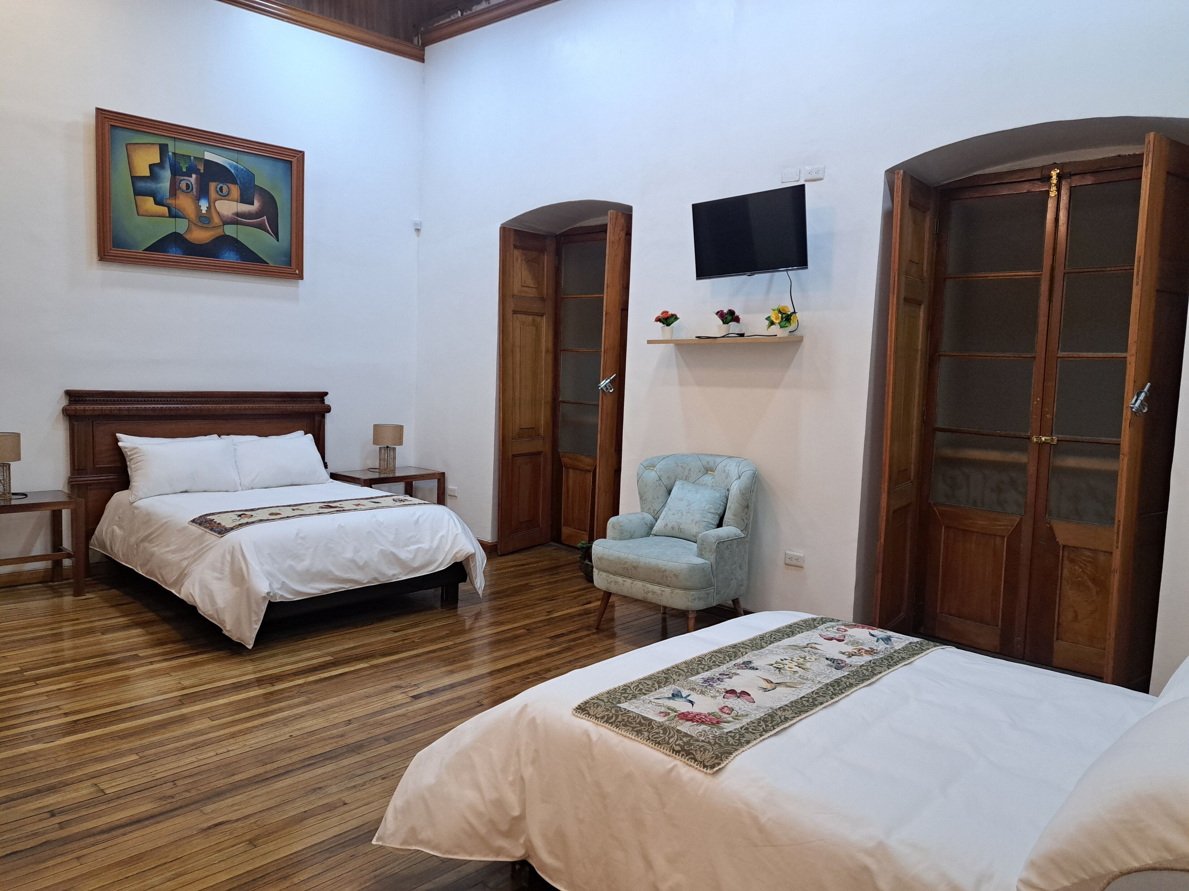 Una habitación de hotel con una cama, una silla, un televisor y un cuadro en la pared.