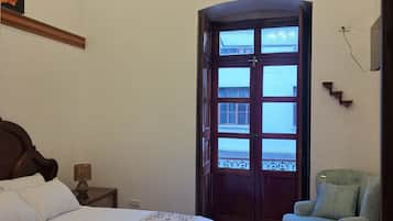 Un dormitorio con cama, una silla, una puerta con ventanas, una lámpara en el techo y un enchufe en la pared.