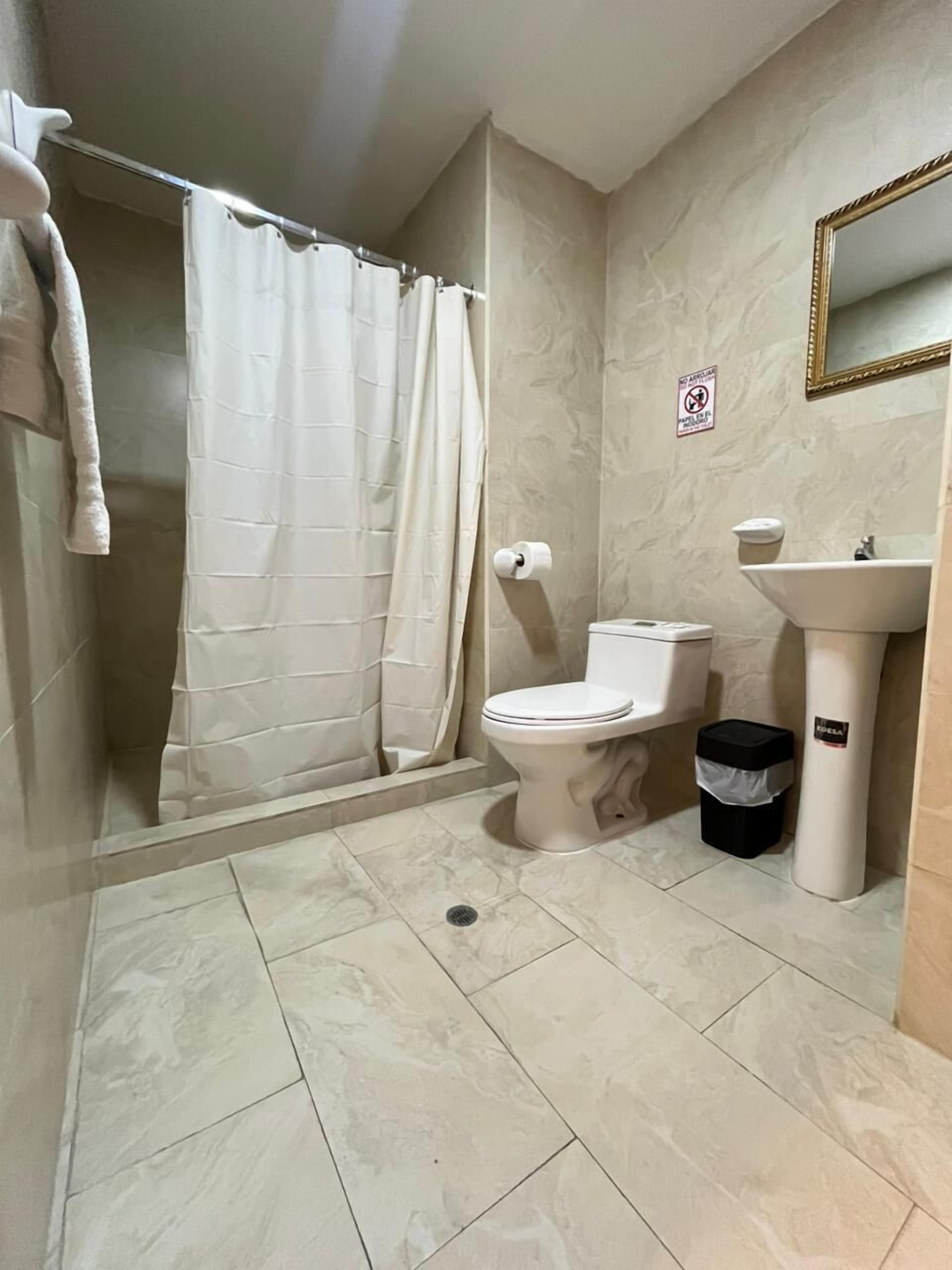 Baño con ducha, inodoro, lavamanos y un cubo de basura.