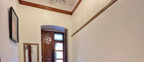 A hallway with a wooden floor, a red leather sofa, a wooden door, a mirror, and a chandelier.