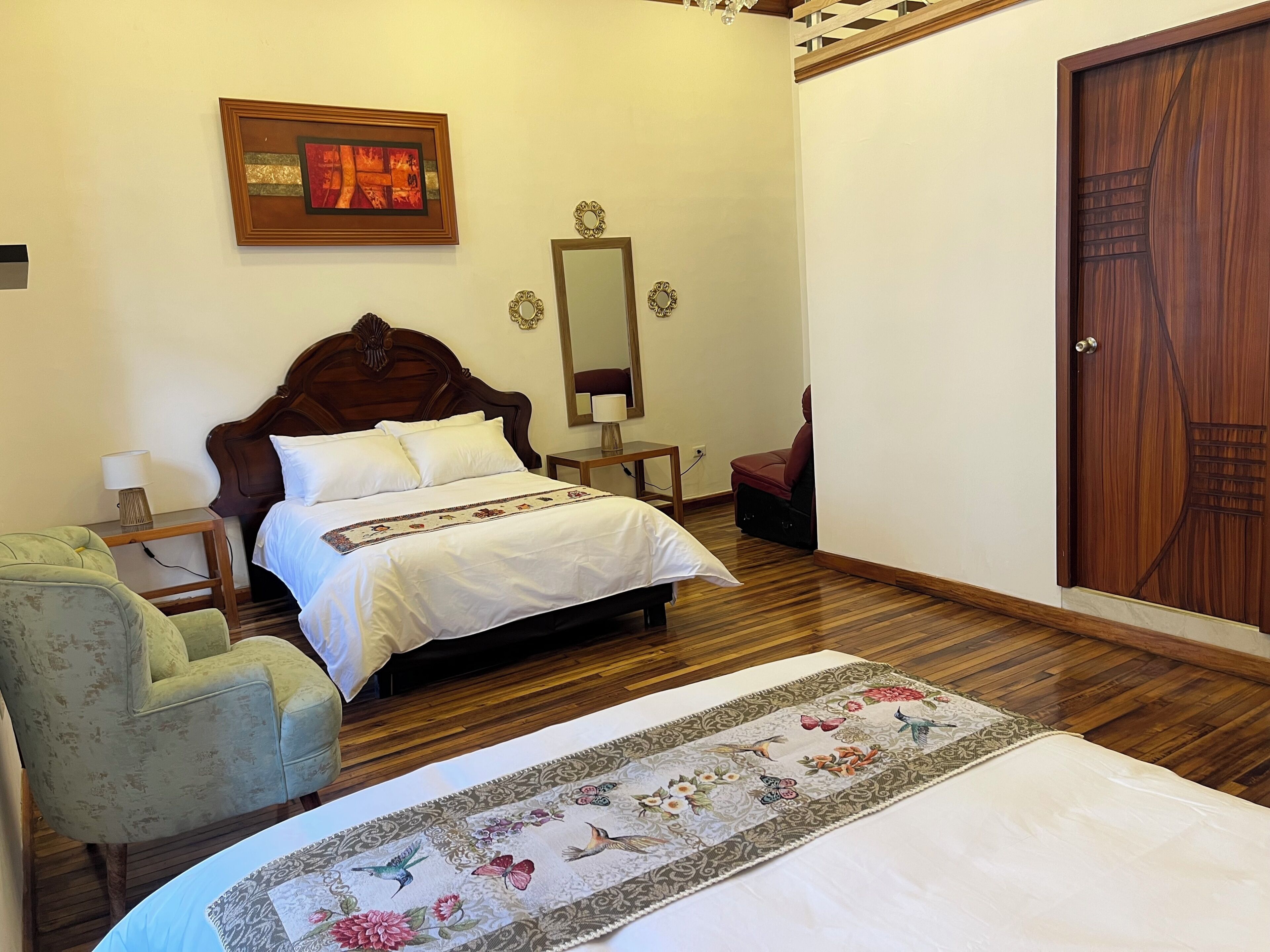 A bedroom with a wooden bed, a green armchair, a wooden wardrobe, and a mirror on the wall.