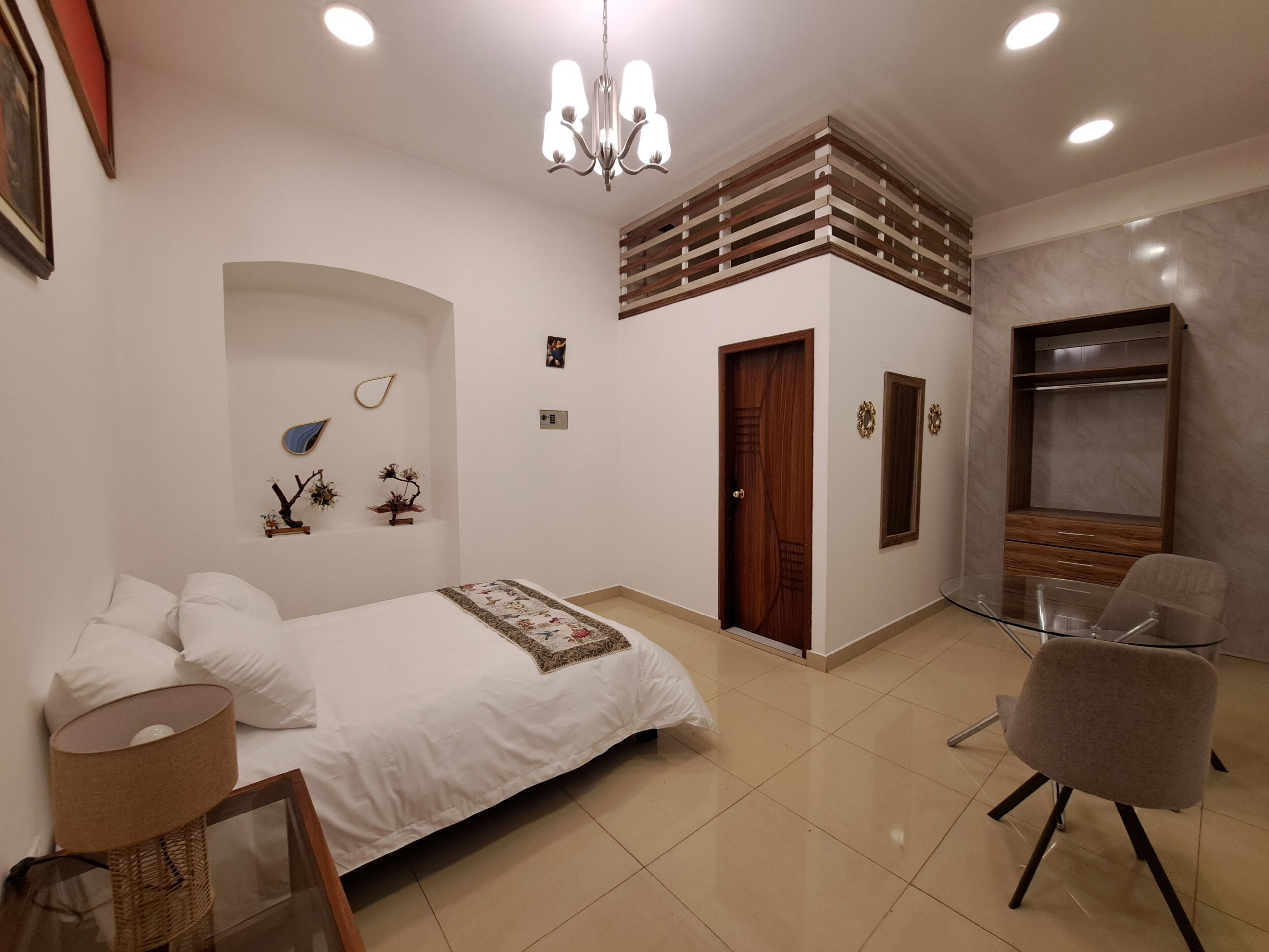 Un dormitorio moderno con cama, una silla, un escritorio, una araña y un armario.