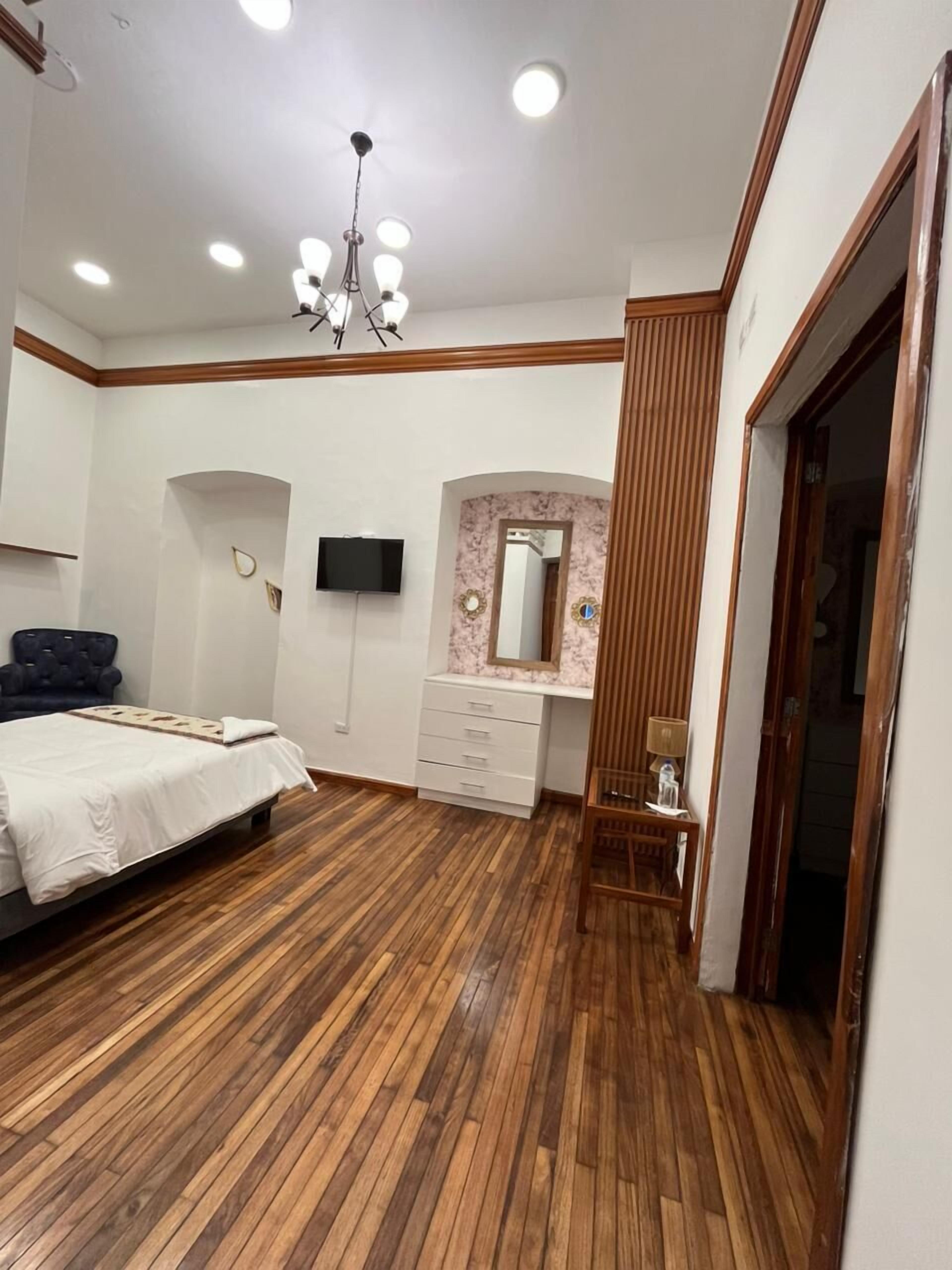 Un dormitorio con cama, televisor, tocador con espejo y suelo de madera.