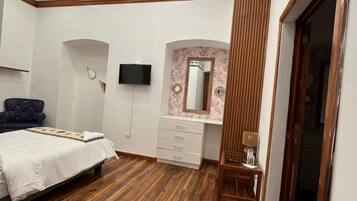 Un dormitorio con cama, televisor, tocador con espejo y suelo de madera.