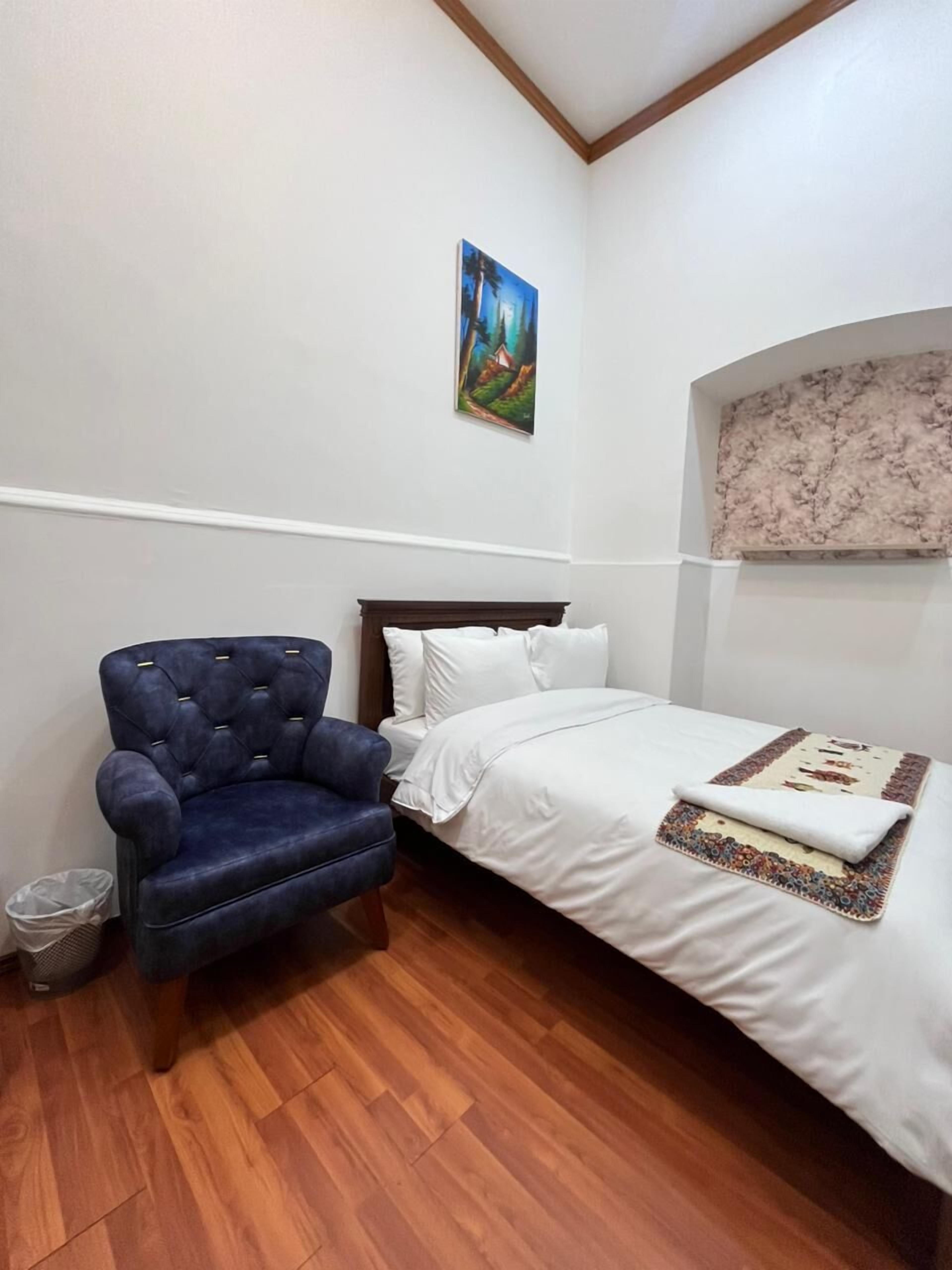 Quarto com cama, poltrona azul, quadro na parede e painel de parede texturizado.