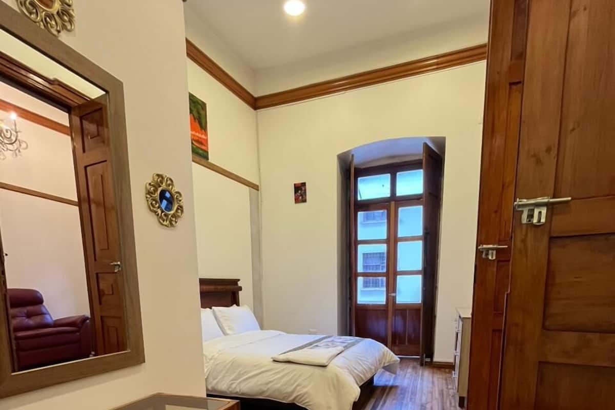 Un dormitorio con piso de madera, cama, escritorio y un espejo grande.