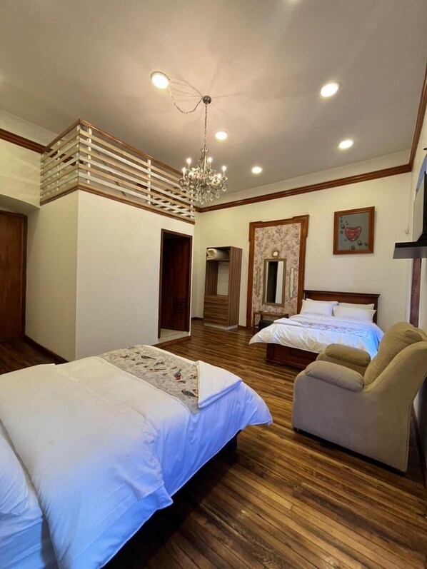 A bedroom with two beds, a chandelier, wooden flooring, and a wooden staircase. - Rossa Mia Hotel Boutique (Quito)