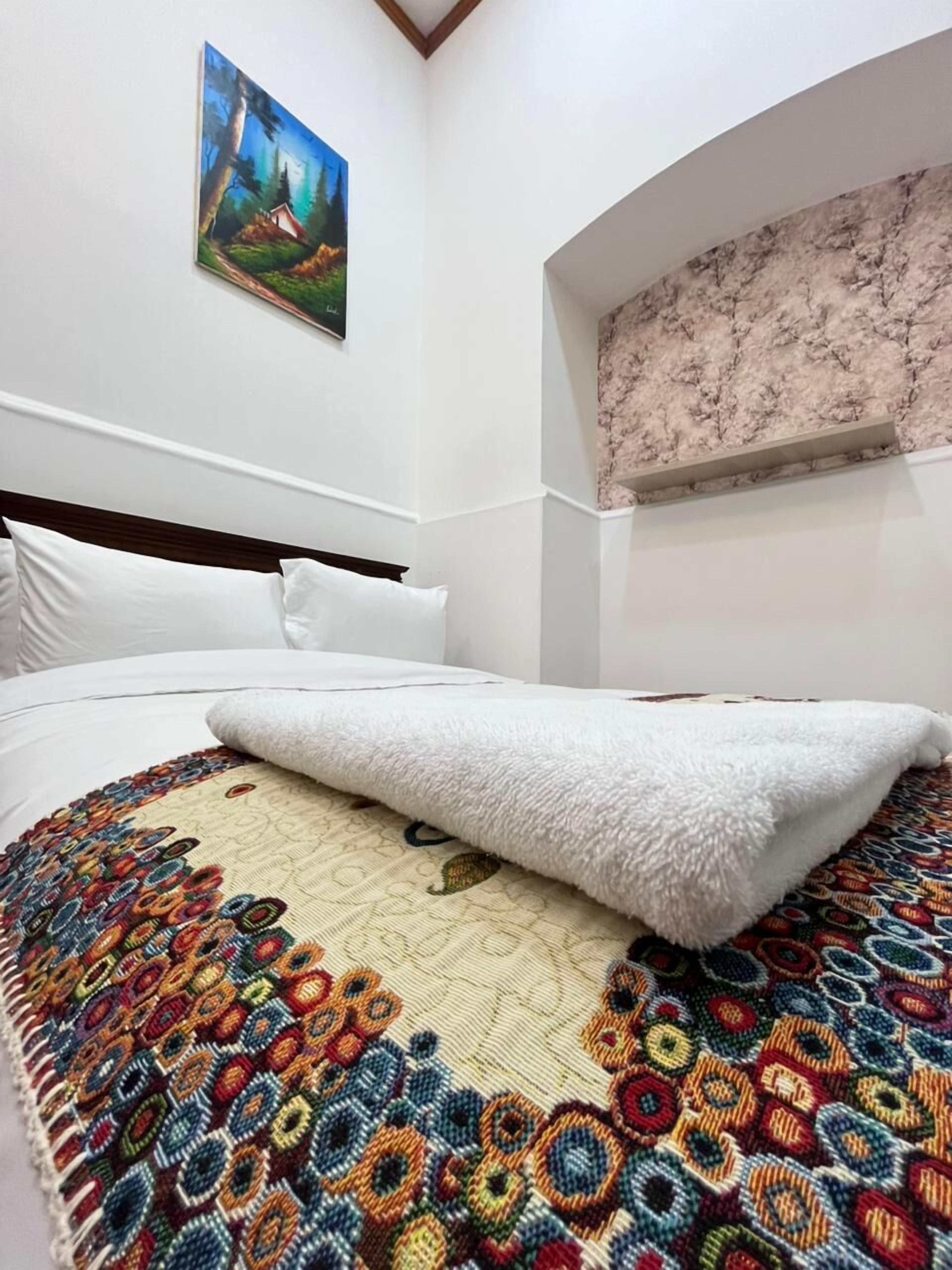 A bed with a colorful, patterned bedspread and a white, fluffy blanket.