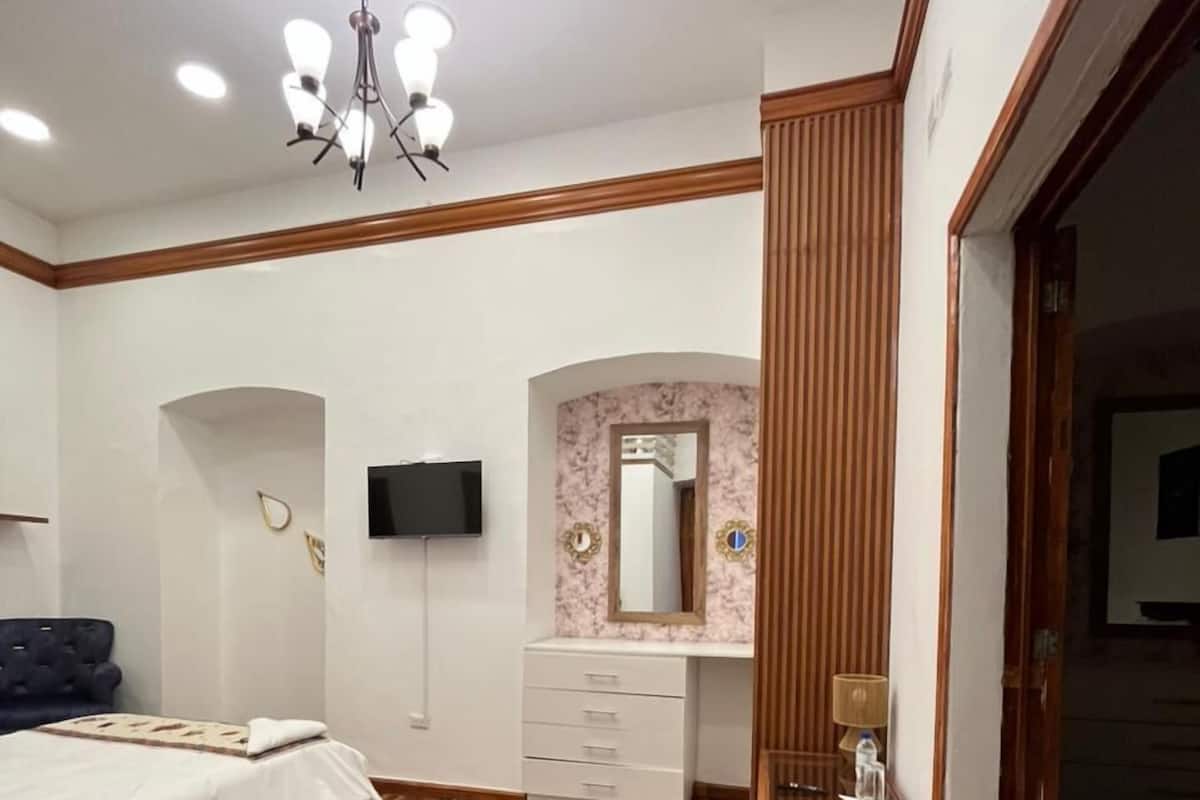 Un dormitorio con cama, televisor, tocador con espejo y piso de madera.